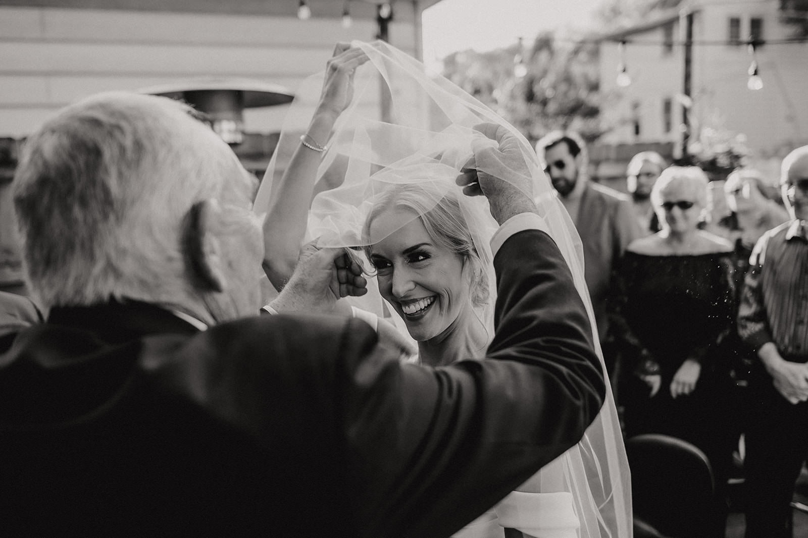 Documentary wedding photography moment of a parent lifting the bride’s veil before the ceremony in black and white